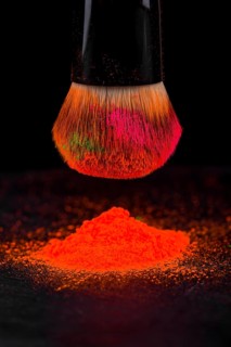 Cheek brush with neon cosmetic powder colorful pile and isolated on black background