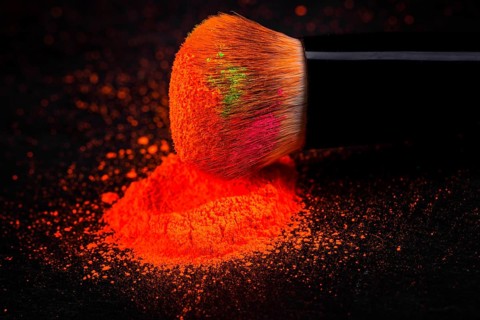 Cheek brush with neon cosmetic powder colorful pile and isolated on black background