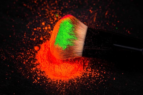 Cheek brush with neon cosmetic powder colorful pile and isolated on black background