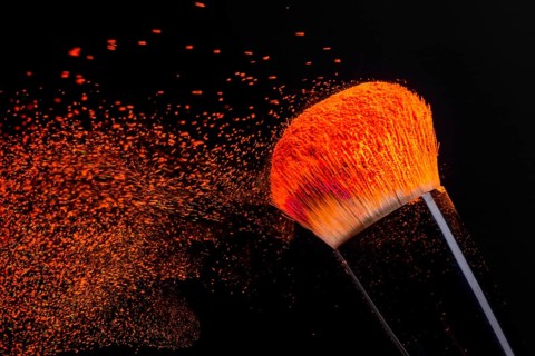 Cheek brush with neon cosmetic powder colorful spray and isolated on black background