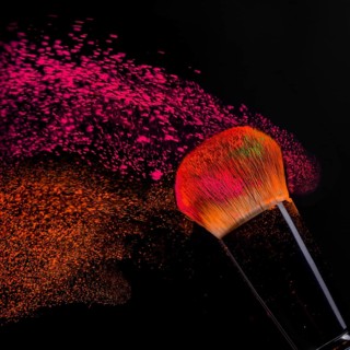 Cheek brush with neon cosmetic powder colorful spray and isolated on black background