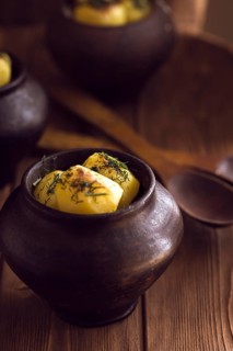Baked potato in old pot on wooden background with pickled cabbage and cucumber