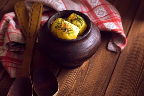 Baked potato in old pot on wooden background with pickled cabbage and cucumber