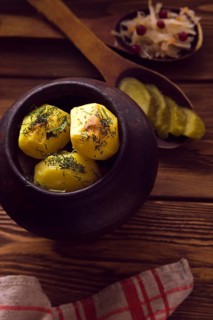 Baked potato in old pot on wooden background with pickled cabbage and cucumber