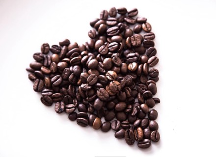 Grains of roasted coffee in the shape of heart on a white plate