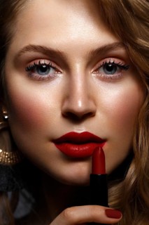 Beautiful girl with red lips and classic makeup and curls with lipstick in hand. Beauty face. Photo taken in the studio