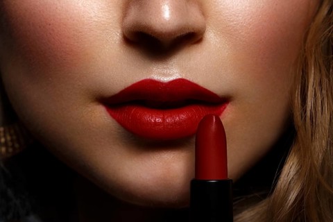 Beautiful girl with red lips and classic makeup and curls with lipstick in hand. Beauty face. Photo taken in the studio