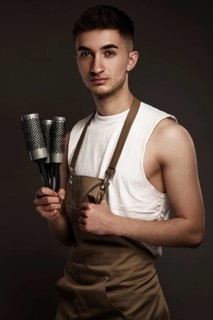 Handsome man hairdresser in a working uniform with brushing combs in his hands. Photo taken in the studio