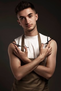 Handsome man hairdresser in a working uniform with scissors in his hands. Photo taken in the studio