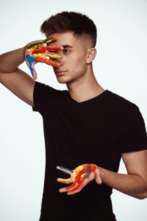 A young man with multi-colored paint on his hands. Hairdresser colorist or artist