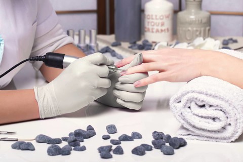 Closeup finger nail care by manicure specialist in beauty salon. Manicurist clear cuticle professional electric tool for manicure and pedicure