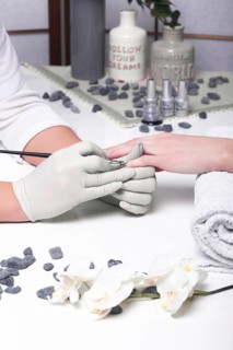 Closeup finger nail care by manicure specialist in beauty salon. Manicurist paints nails with nail polish