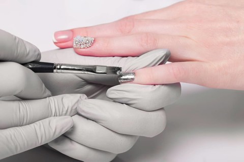 Closeup finger nail care by manicure specialist in beauty salon. Manicurist paints nails with nail polish