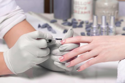 Closeup finger nail care by manicure specialist in beauty salon. Manicurist paints nails with nail polish