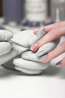 Closeup finger nail care by manicure specialist in beauty salon. Manicurist paints nails with nail polish