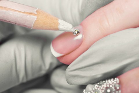 Closeup finger nail care by manicure specialist in beauty salon. Manicurist Glues rhinestones on nails