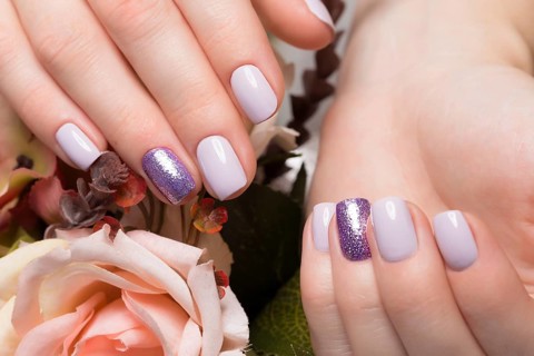 Purple neat manicure on female hands on a background of flowers. Nail design