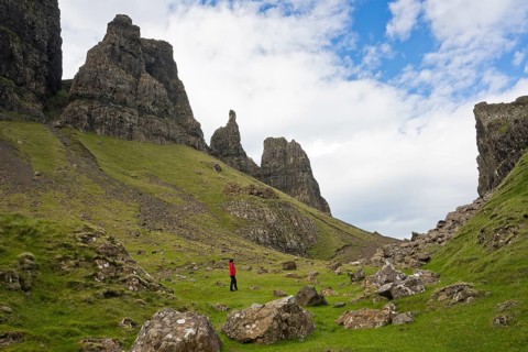 Hiker in red outdoor jacket in the bizarre rock world of Quiraing