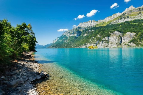 View from the shore of Lake Walen of the small chive island in the middle of the turquoise water at the foot of the Churfirsten and with the Schaeren mountain range in the background