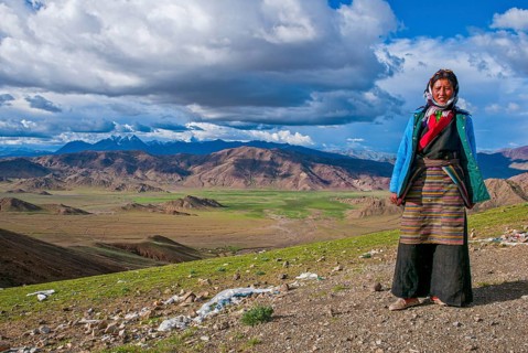 Tibetan woman posing before the mountainous Himalaya landscape along the southern route into Western Tibet