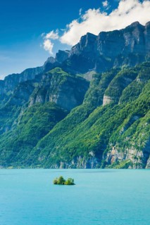 Sunny view over Lake Walen with the small chive island in the turquoise water and mountain range Schaeren and Leistchamm in the background