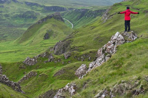 Hiker in red outdoor jacket in the bizarre rock world of Quiraing