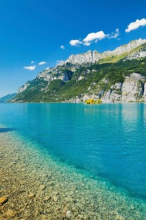 View from the shore of Lake Walen of the small chive island in the midst of the turquoise water and with the mountain range Schaeren and Leistchamm in the background