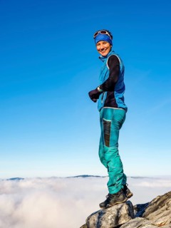Mountaineer standing exposed on a rock above the clouds