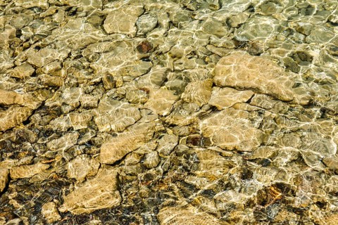 Sun casts fascinating play of light and shadow on the clear water and beige-brown stones on the shore of Lake Walen