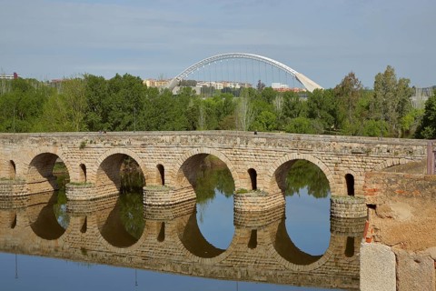 Roman stone arch bridge Puente Romano with reflection in the river Rio Guadiana and modern arch bridge Puente Lusitania