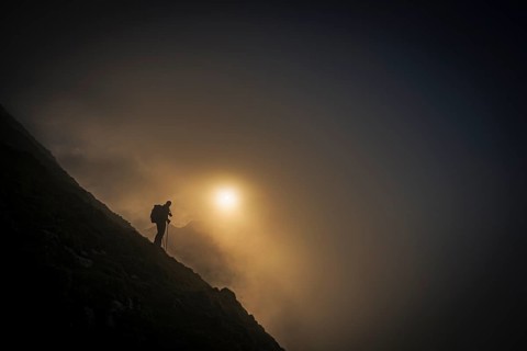 Mountaineer on mountain slope with fog against the light