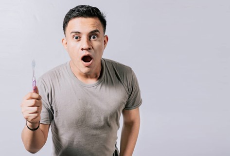 Guy holding toothbrush with amazed face isolated on white