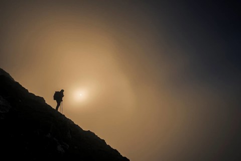 Mountaineer on mountain slope with fog against the light