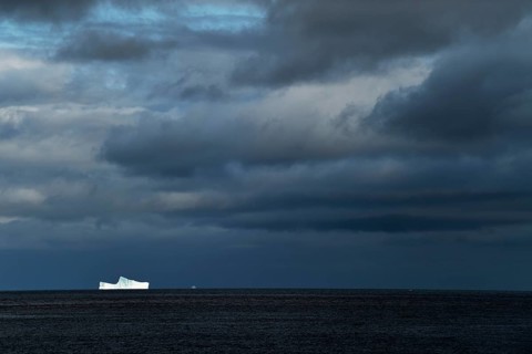Iceberg drifting on the open sea against a dark cloudy sky