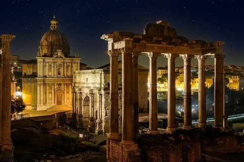 View of right Temple of Saturn of Roman religion centre Arch of Severus on Roman Forum left background Church of Santi Luca e Martina under starry sky night sky with stars