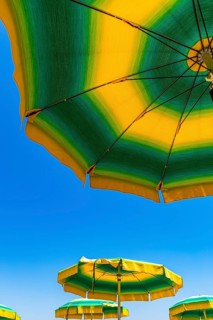 Green-yellow parasols against a blue sky on the beach of Straccoligno