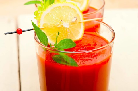 Fresh tomato juice gazpacho soup on a glass over white wood table
