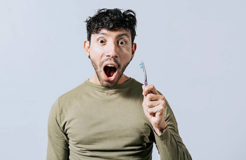 Surprised young man holding a toothbrush. Amazed teenager holding toothbrush isolated
