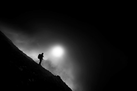Mountaineer on mountain slope with fog against the light