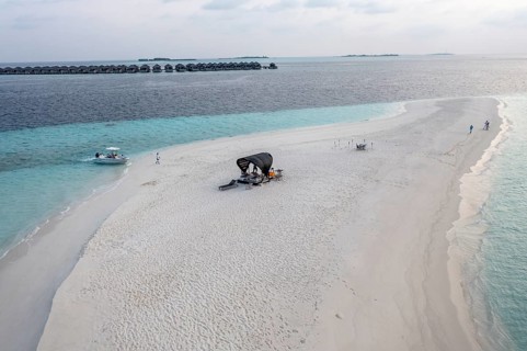 Aerial view: lonely sandbank in the Maldives with a table and sun loungers for romantic dinners
