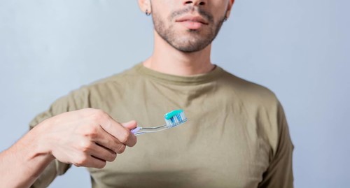 Guy with unrecognizable face holds brush with toothpaste on isolated background