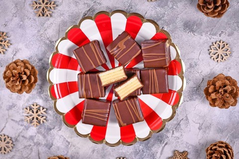 German layered winter cake pralines called Baumkuchen on striped plate next to seasonal pine cones and wooden snowflake ornaments