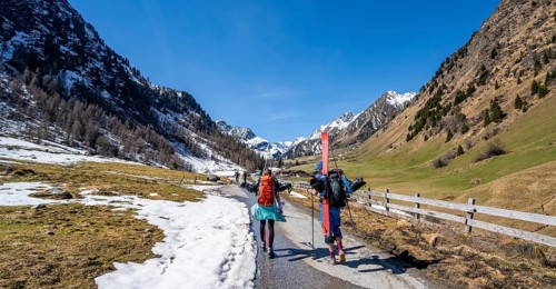 Ski tourers carrying skis on their backpacks with little snow in spring