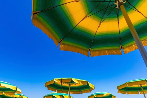 Green-yellow parasols against a blue sky on the beach of Straccoligno
