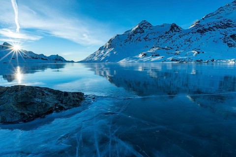 Ice structures and rock in the black ice of the frozen Lago Bianco in the Swiss mountains