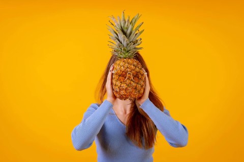 A pineapple in sunglasses in a studio on a yellow background