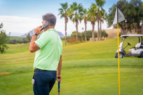 Young businessman playing golf and answering a work call with the phone from the club