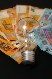 Lighted light bulb with euro banknotes in the background on a black background