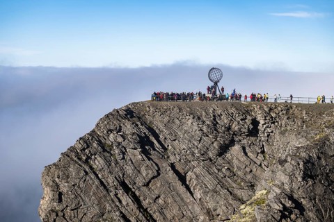 Rock cliff of the North Cape with steel globe at midnight sun