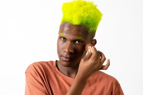 An androgynous black man posing putting on makeup